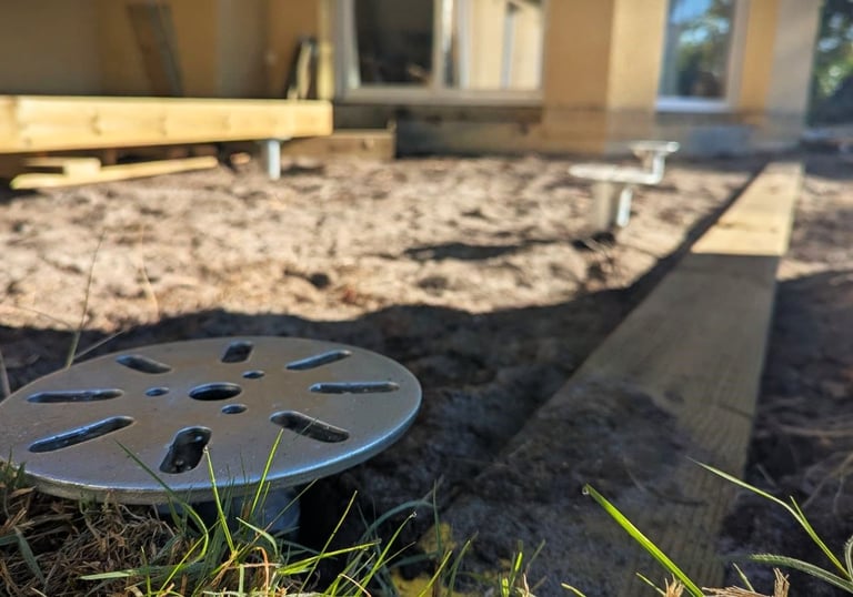 Adjustable steel screw piles installed in dirt for a backyard deck construction project.