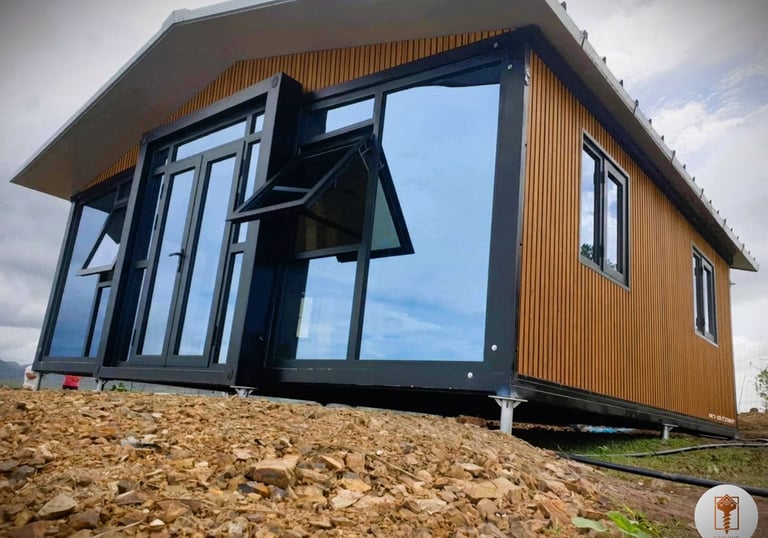 Modern prefabricated modular cabin with wood siding and large glass windows on a rocky foundation.