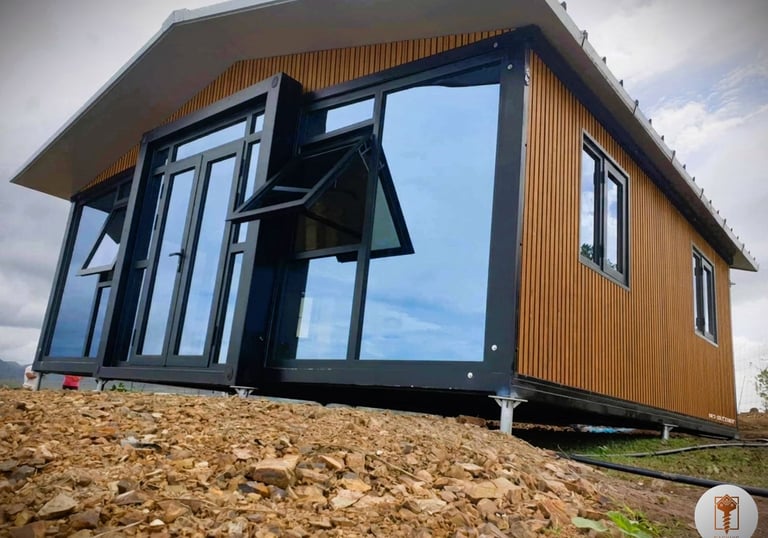 Modern prefab container home with wood siding and large glass windows on a rocky hill.