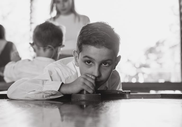 a boy is sitting at a table with his hands on his chin