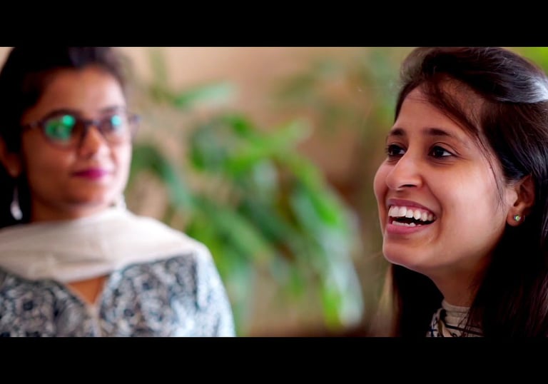 a woman with glasses and a scarf looking at another woman who is smiling