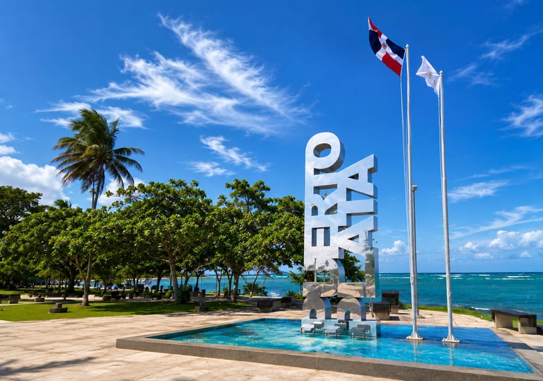 Puerto Plata sign and Dominican Republic flag at a tropical oceanfront park.