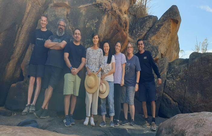 a group of people standing in front of a large rock formation - going out for bush walk