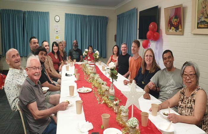 a group of people sitting at a long table - celebrating Christmas