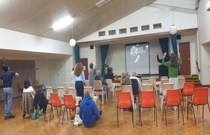 a group of people standing in a room with chairs and a projector - worship encounter night