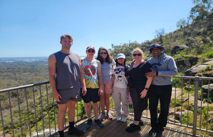 A group of people standing on a lookout platform overlooking a valley and hills