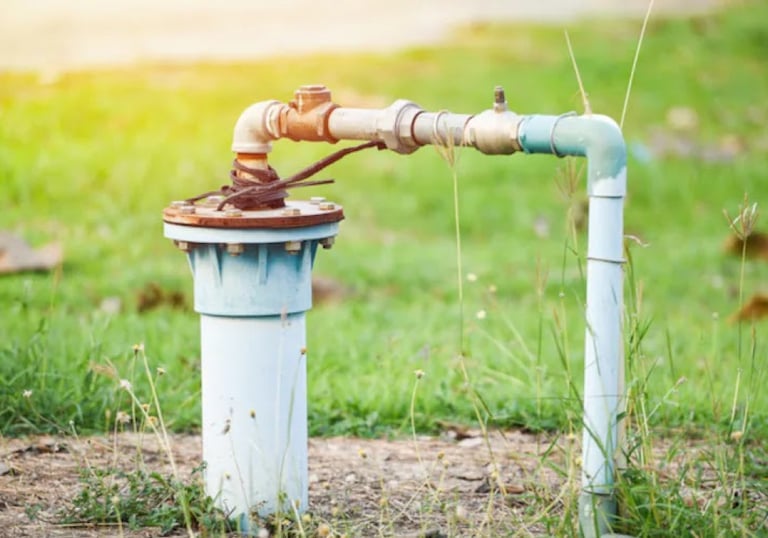 Outdoor water well pump head and pvc pipe plumbing installation in a green grass field.