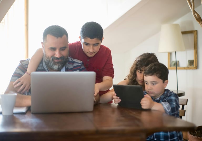 "Dad on computer with wife and kids nearby, representing ADHD parent coaching at home