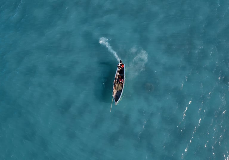 Location: Anse La Raie. Aerial view of a boat gliding across the clear blue waters of Mauritius, with two fishermen onboard