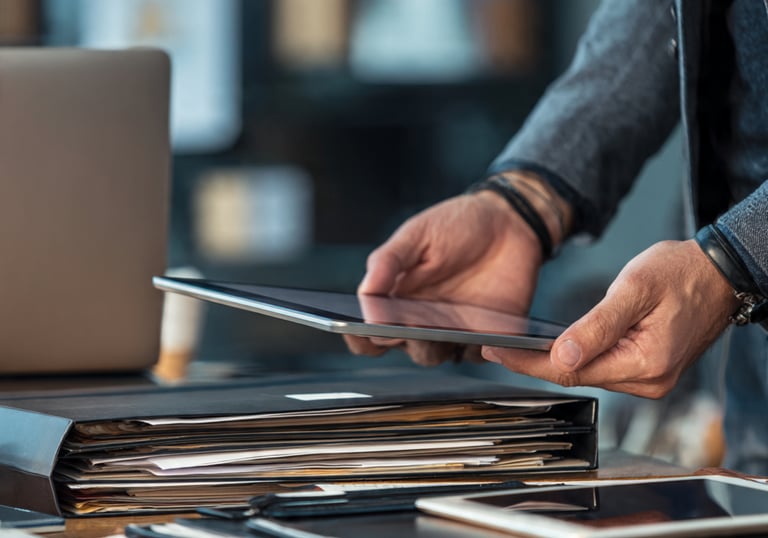 Professional person using a digital tablet above a desk with document folders and a laptop.