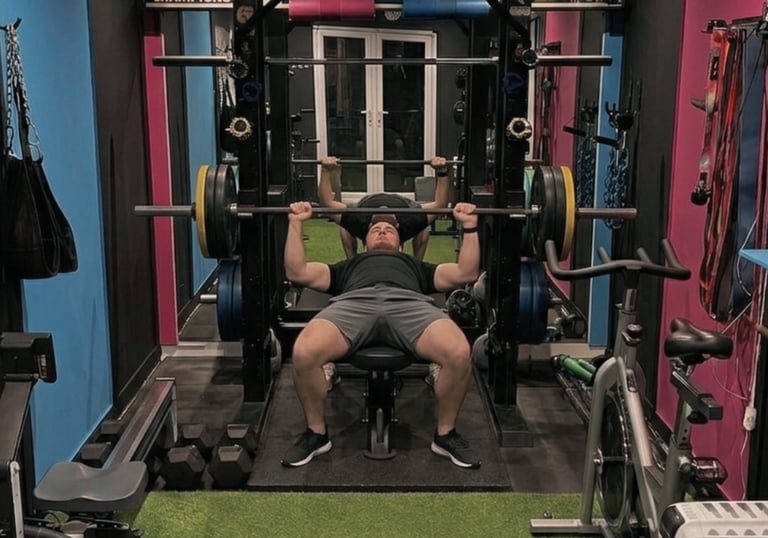 A client performing a barbell bench press in Robb Sheridans gym with a power rack and weights.