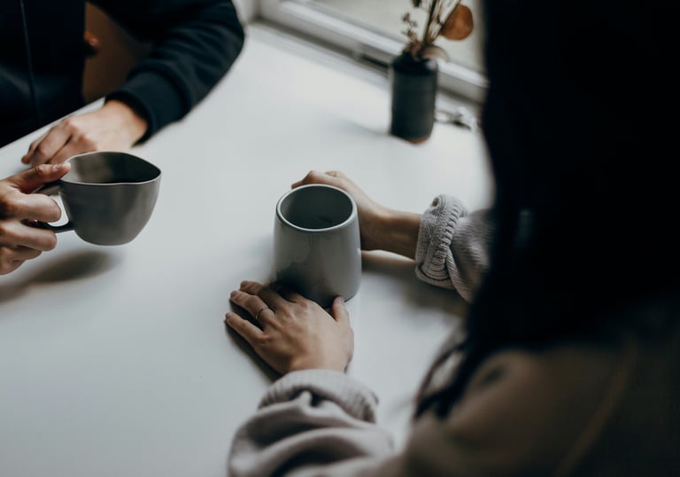 a therapist and client sit at a table, drinking coffee, having a private and empowering conversation