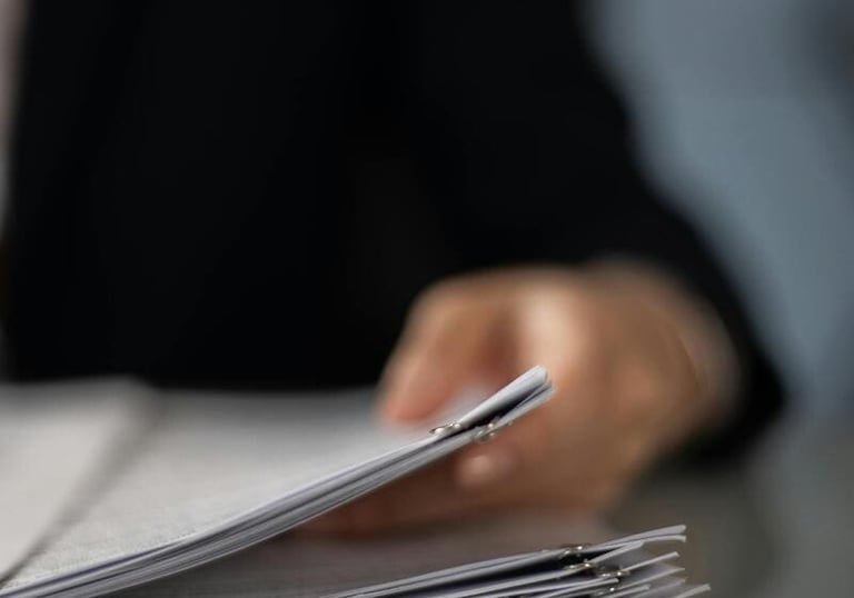 Un profesional revisa una pila de documentos en papel organizados en un escritorio.