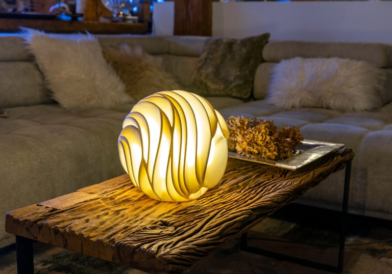 A modern spherical sculptural lamp glowing on a rustic wooden coffee table in a cozy living room.