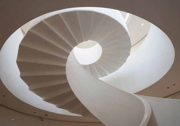 A low-angle view of a clean, modern spiral staircase in a North American gallery, emphasizing elegant movement and strategic progression.
