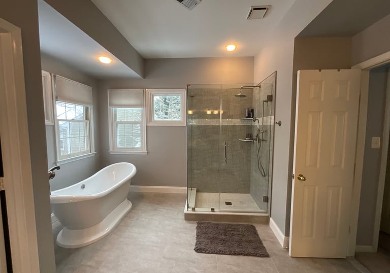 Renovated bathroom with white freestanding bathtub, stainless steel tub filler, and glass shower