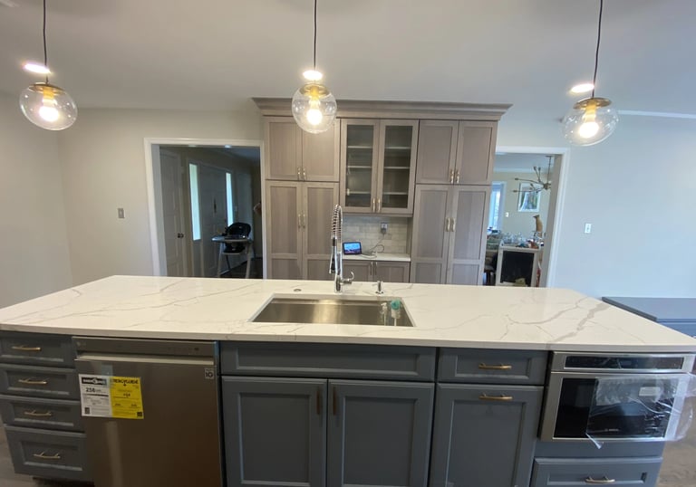 Remodeled kitchen island in dark gray with white veined quartz and light gray cabinets.