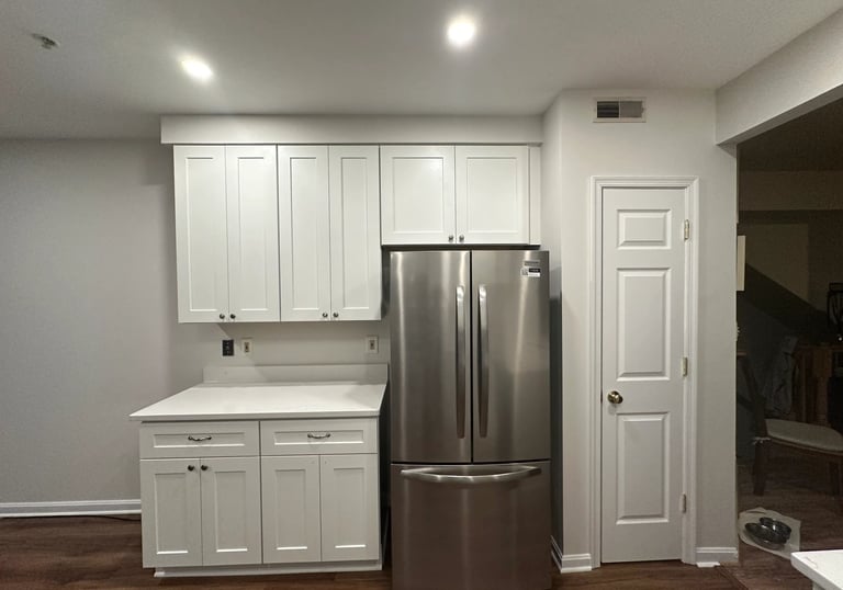 Kitchen remodel with white cabinets, stainless steel fridge, and modern white door.