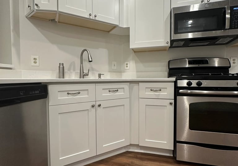 Kitchen remodel detail: white cabinets with stainless steel microwave, oven, and dishwasher.