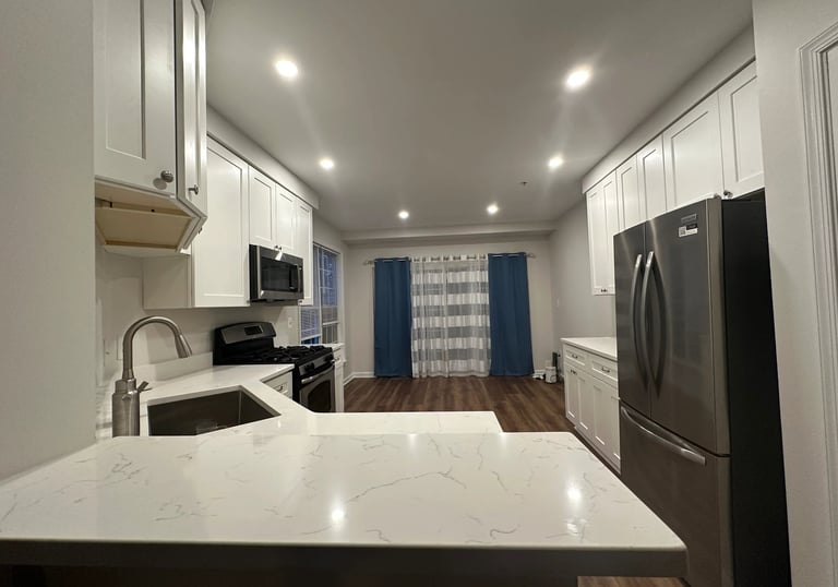 Renovated kitchen with white shaker cabinets, quartz counters, and a stainless steel fridge.