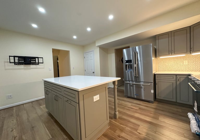 Grey kitchen remodel with large white quartz island, steel fridge, and light brown LVP floors.
