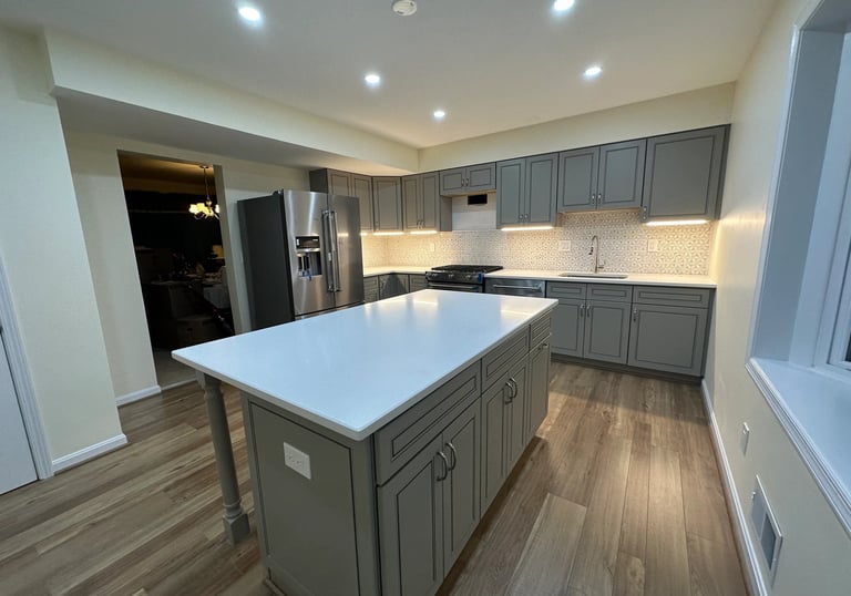 Full view of a bright kitchen remodel with grey cabinets, brown LVP floors, and window.