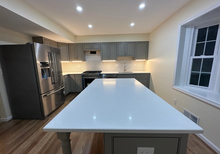 Long view of a grey kitchen remodel with large white island and light brown LVP floor.
