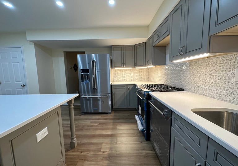 Remodeled kitchen view with grey cabinets, steel fridge, and multi-tonal brown LVP floors.