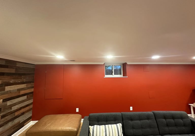 Newly renovated basement wall painted red with small window, white crown molding, and gray sofa.