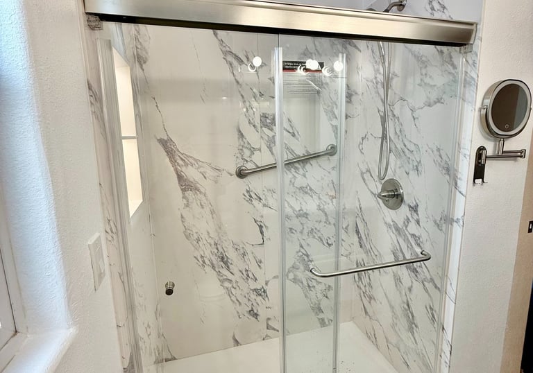Modern walk-in shower with white marble wall tiles, sliding glass doors, and ADA compliant grab bars.