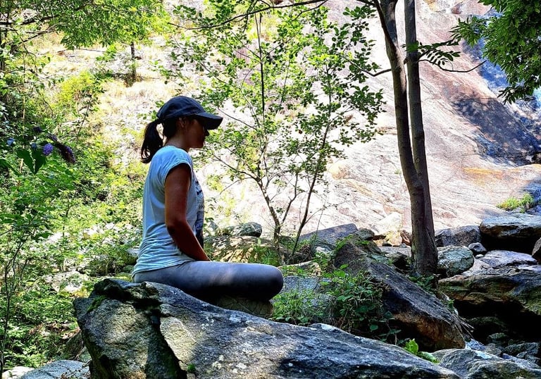 donna seduta su scoglio in meditazione con alberi e cascata
