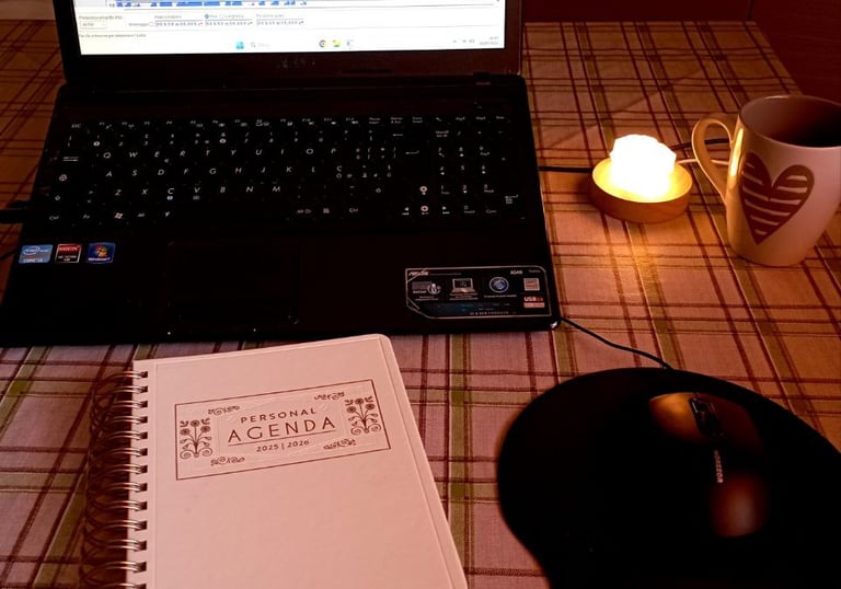 tavola con sopra agenda, computer che ostra programma di registrazione, lampada con luce soffusa e tazza di tisana