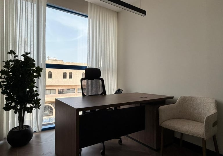 Modern office interior with a wooden executive desk, mesh chair, and large window with white curtains.