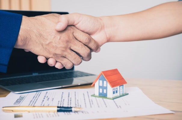 Agente inmobiliario dándose la mano sobre un modelo de contrato para comprar o rentar propiedad