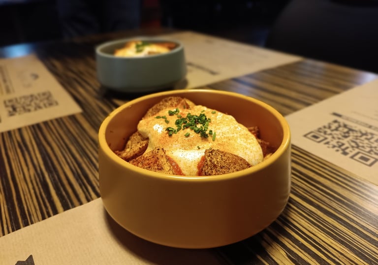 Crispy patatas bravas topped with creamy aioli and fresh chives in a yellow ceramic bowl.