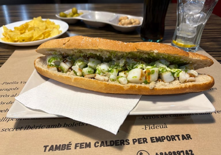 Grilled cuttlefish sandwich with green parsley garlic oil served on a baguette with side snacks.
