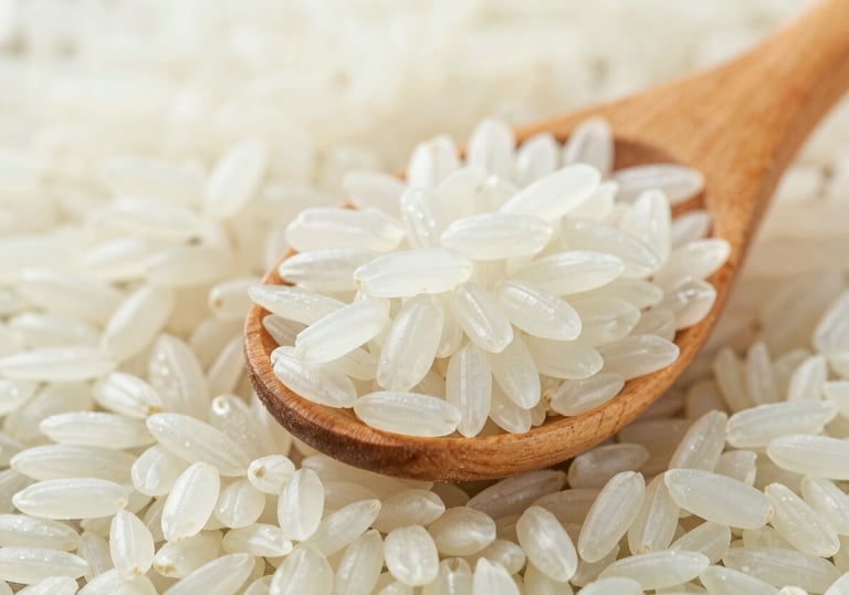 Macro shot of polished Jasmine rice grains held in a wooden scoop, showcasing their long-grain structure and pure white color. Lighting is clean and natural, consistent with #F5F6F3.