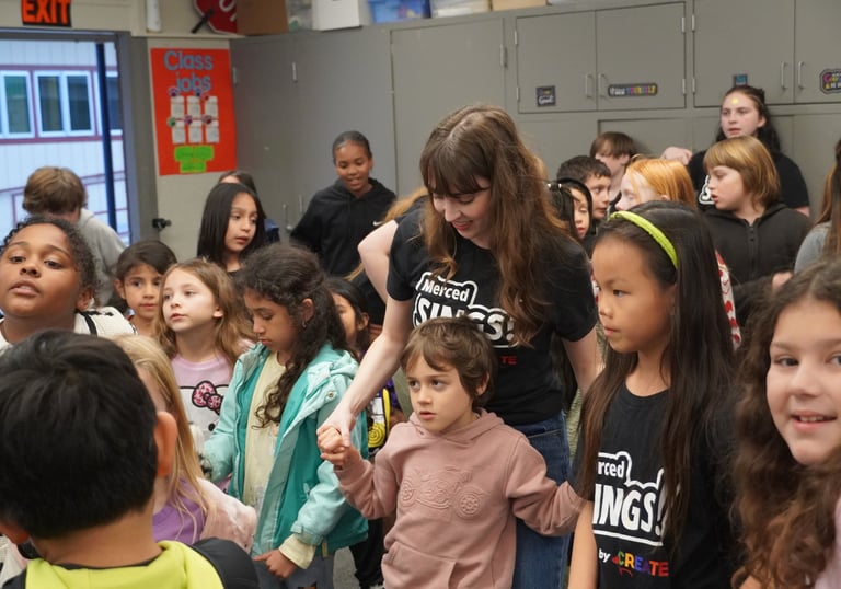 Diverse elementary students and teacher gathered in a classroom for a Merced Sings music program activity.