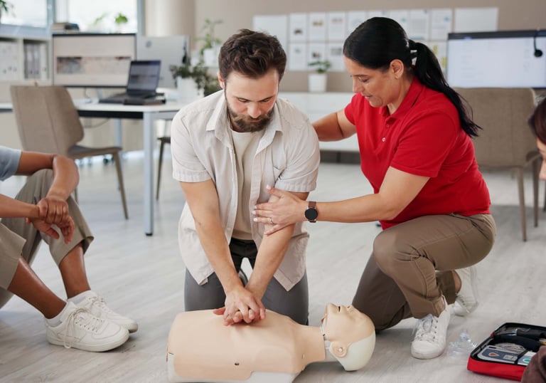Female instructor assisting a male student learning how to perform CPR on a training mannequin