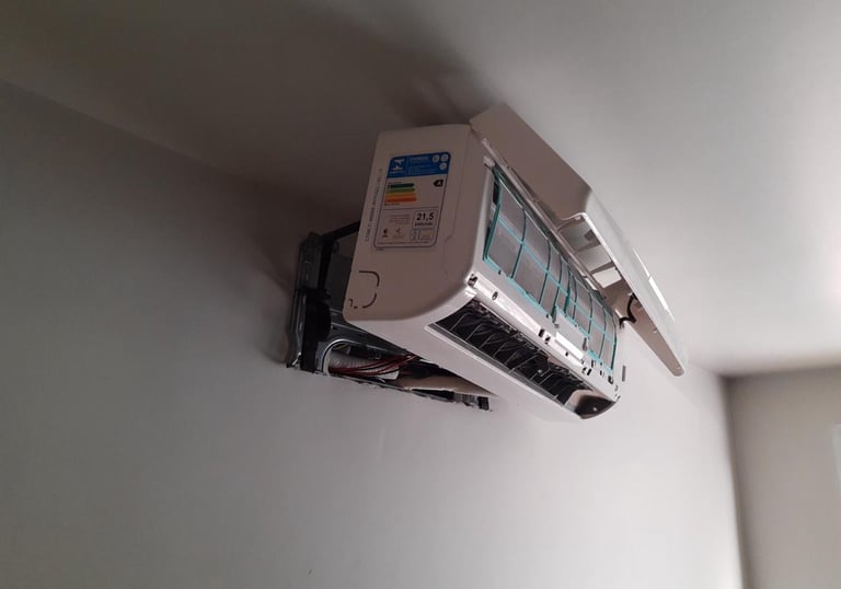 White split air conditioner unit mounted on a wall during maintenance with cover open.