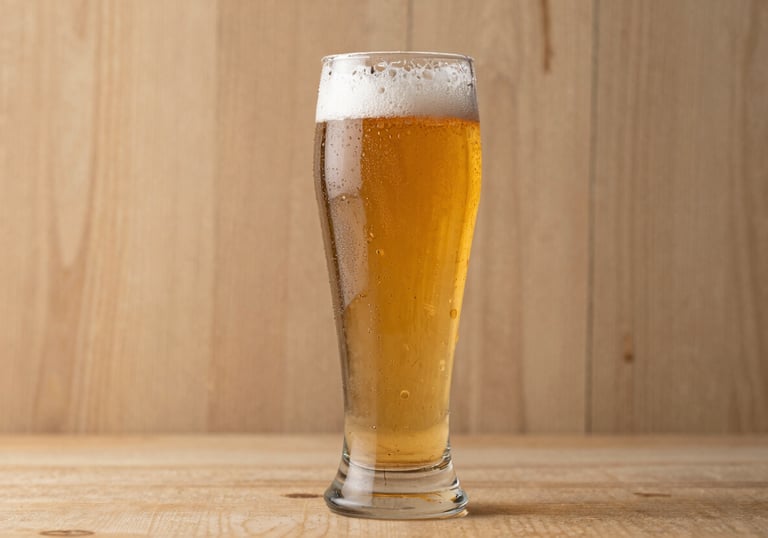 A high-end studio shot of a tall beer glass filled with a golden ale, condensation on the glass. The background is a textured Earthy Tan wood, softly lit.