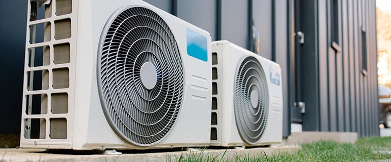 Two modern air conditioning compressor units installed outside a residential home for efficient HVAC cooling.