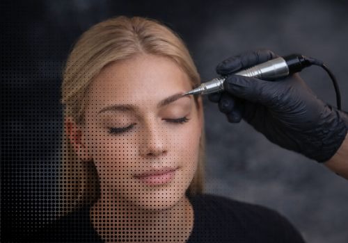 Professional technician performing a permanent makeup eyebrow tattoo procedure on a blonde woman.