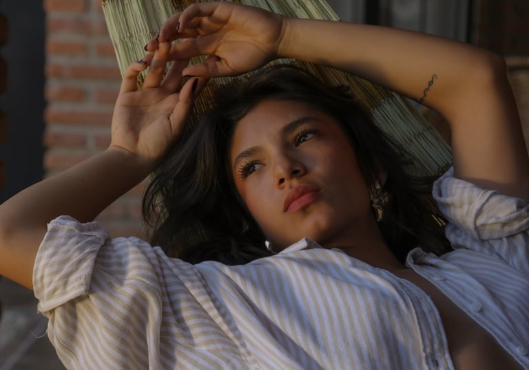 Una joven pensativa con una camisa abierta relajándose en una hamaca tejida al aire libre