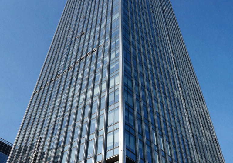 A low-angle shot of a stunning modern glass skyscraper reflecting a royal blue sky. The image emphasizes structural engineering excellence and grand scale. Clean, crisp architectural style.