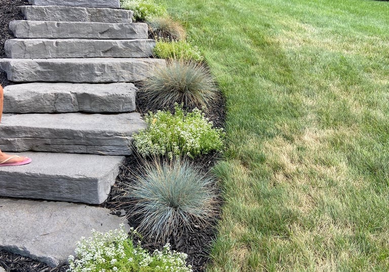Natural stone landscape stairs curving up a green grass hillside with ornamental shrubs.