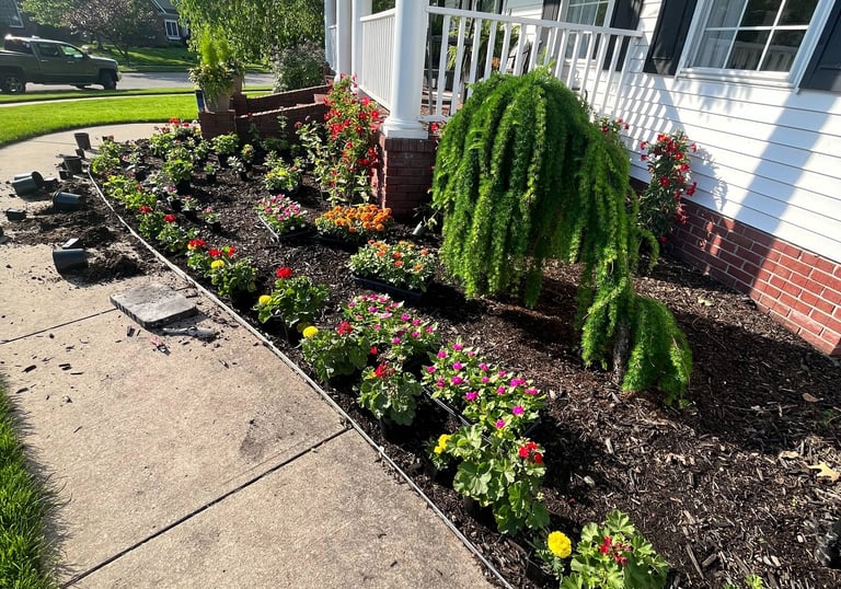 Freshly planted flower bed with colorful annuals and mulch along a white house front porch.