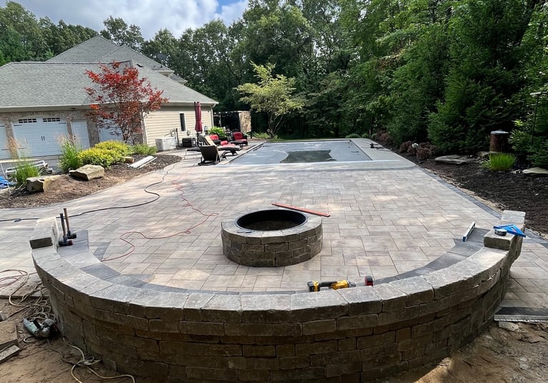 Custom paver patio construction featuring a circular stone fire pit and curved retaining wall seating area.