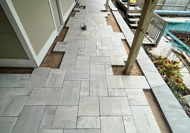 Professional installation of a modern gray stone paver patio under a residential deck.