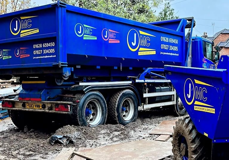 Blue JMC groundworks and demolition tipper truck and site dumper on a muddy construction site.